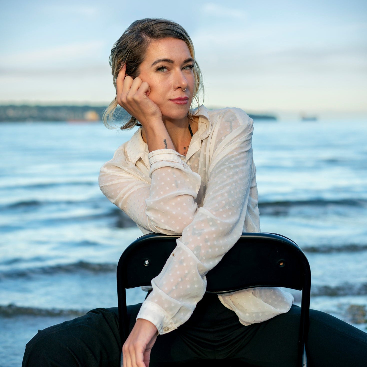 Nicole Scott headshot. She is sitting on a chair by the water with a blurred background.